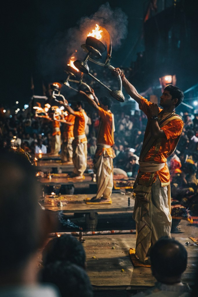 Priests performing the Ganga Aarti ceremony with fire lamps at night on the riverbank